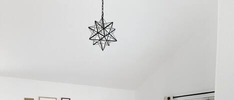 En matplats med ett svart bord, trästolar och en stjärnformad hänglampa. På väggen hänger inramade tavlor och utanför syns grönskan.