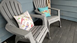 Two grey Adirondack chairs with colorful cushions against a blue wall, on a wooden deck.