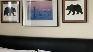 A bedroom with a bed, three framed pictures on the wall, and two pillows with bear designs.