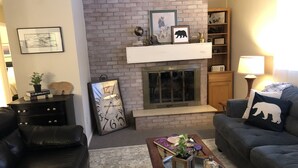 A living room with a fireplace, leather sofas, a coffee table with decorative items, and a bookshelf.