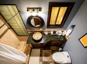 A bathroom with a round mirror, a sink with a bowl, a toilet, and a shower area.