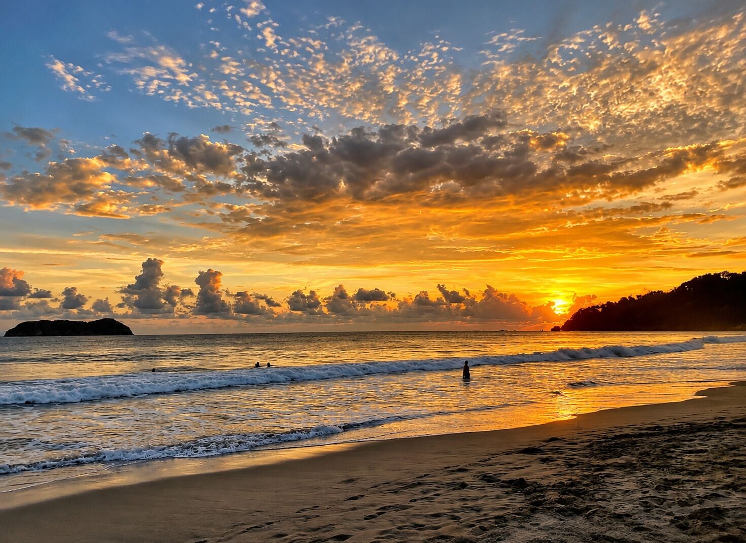 A beach with waves, a sunset, and a distant island.