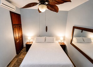 A bedroom with a bed, two bedside tables with lamps, a ceiling fan, and a wall-mounted mirror.
