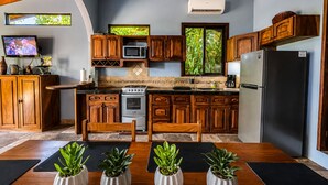 A modern kitchen with wooden cabinets, a stove, microwave, and a refrigerator. - Breathtaking Ocean Vistas, Jungle Bliss, Walk to Eateries & Beach, Fast Internet (Manuel Antonio)