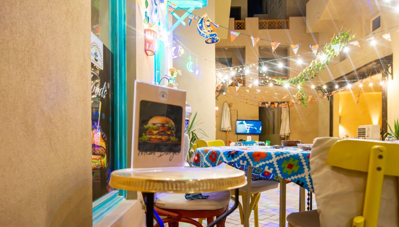 A dining area with tables and chairs, a television, and decorative lights.
