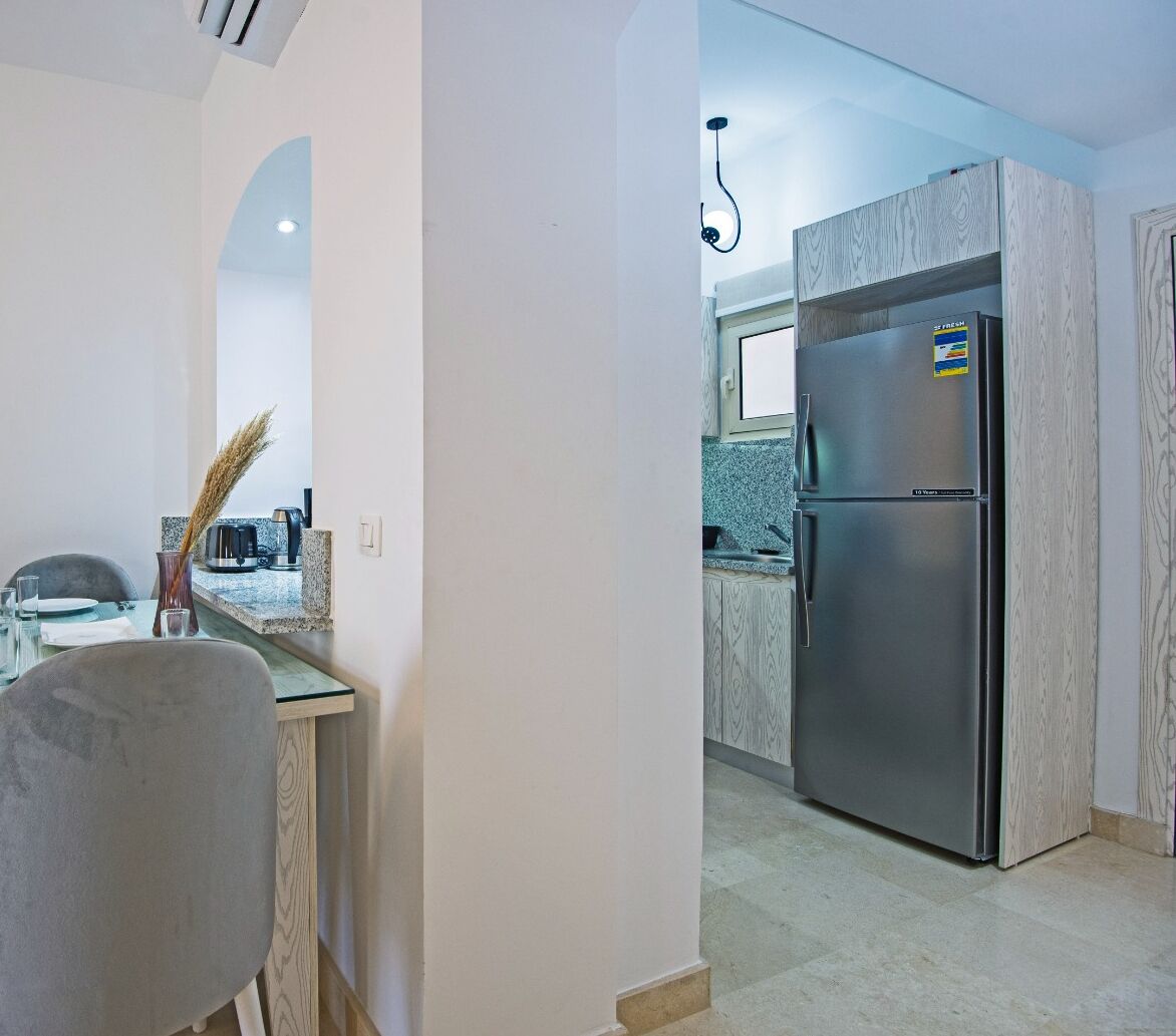 A modern kitchen with a stainless steel refrigerator, granite countertops, and a dining area with a glass table and chairs.