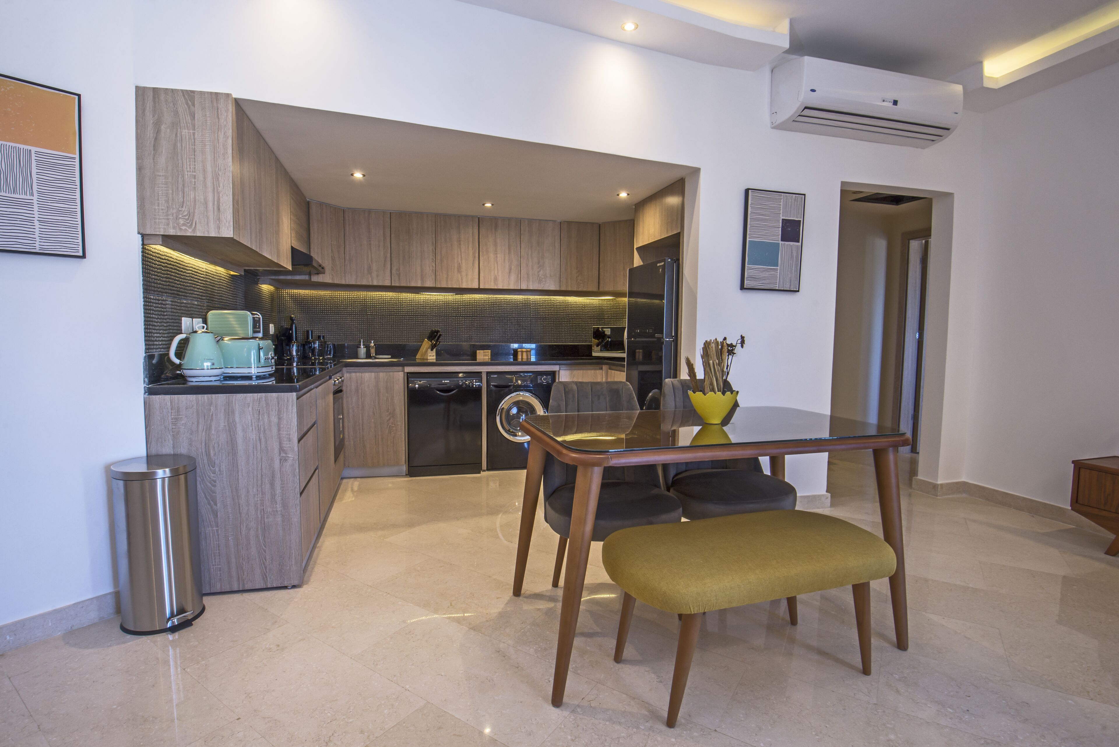 A modern kitchen with a dining area, featuring a glass table and wooden chairs.