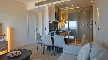 Una sala de estar moderna con un sofá, sillas, una mesa de centro y una cocina visible a través de una puerta de vidrio.