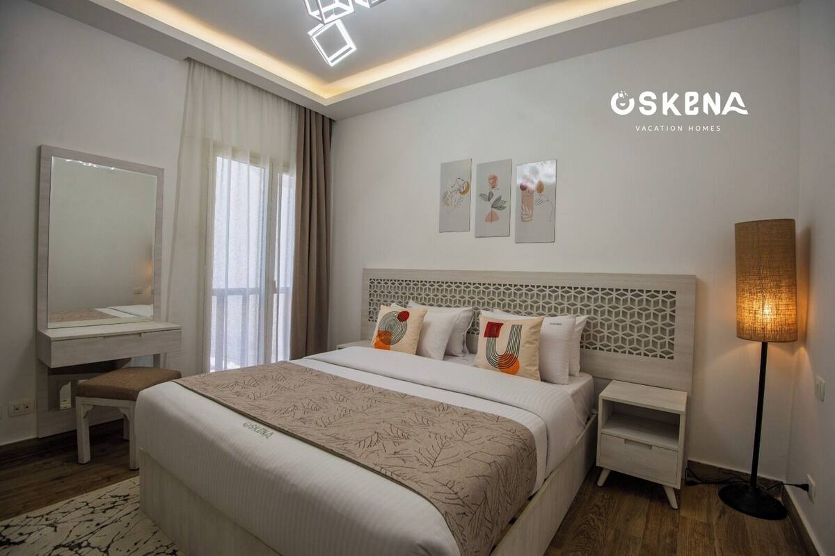A modern bedroom with a large bed, bedside tables, a mirror, and a floor lamp.