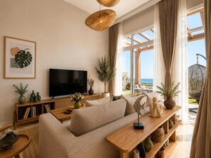 Een moderne woonkamer met een grote flatscreen-tv, een bank, een houten salontafel en uitzicht op de oceaan door grote ramen.