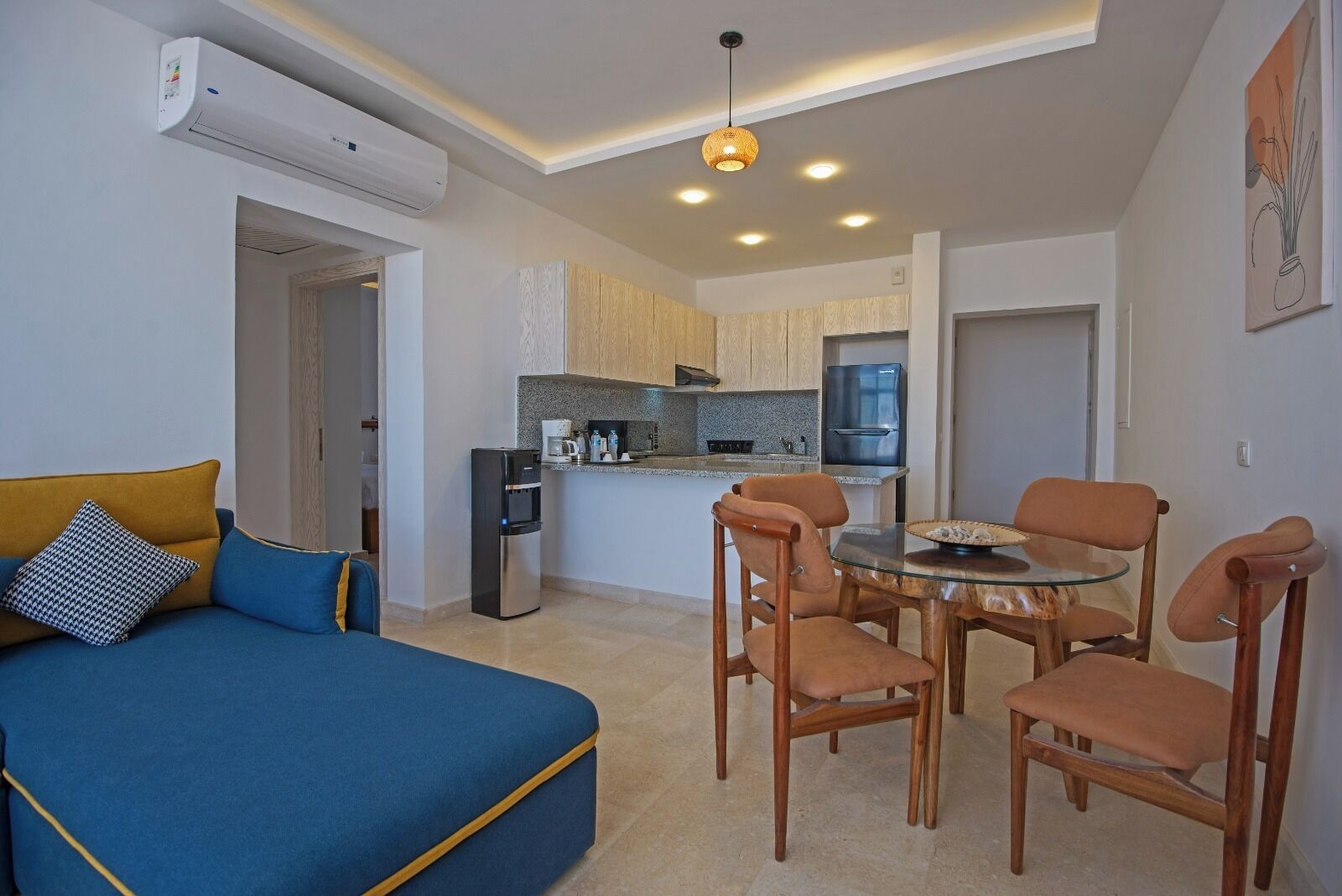 Un espacio habitable compacto con sofá, mesa de comedor y sillas, kitchenette y aire acondicionado instalado en el techo.