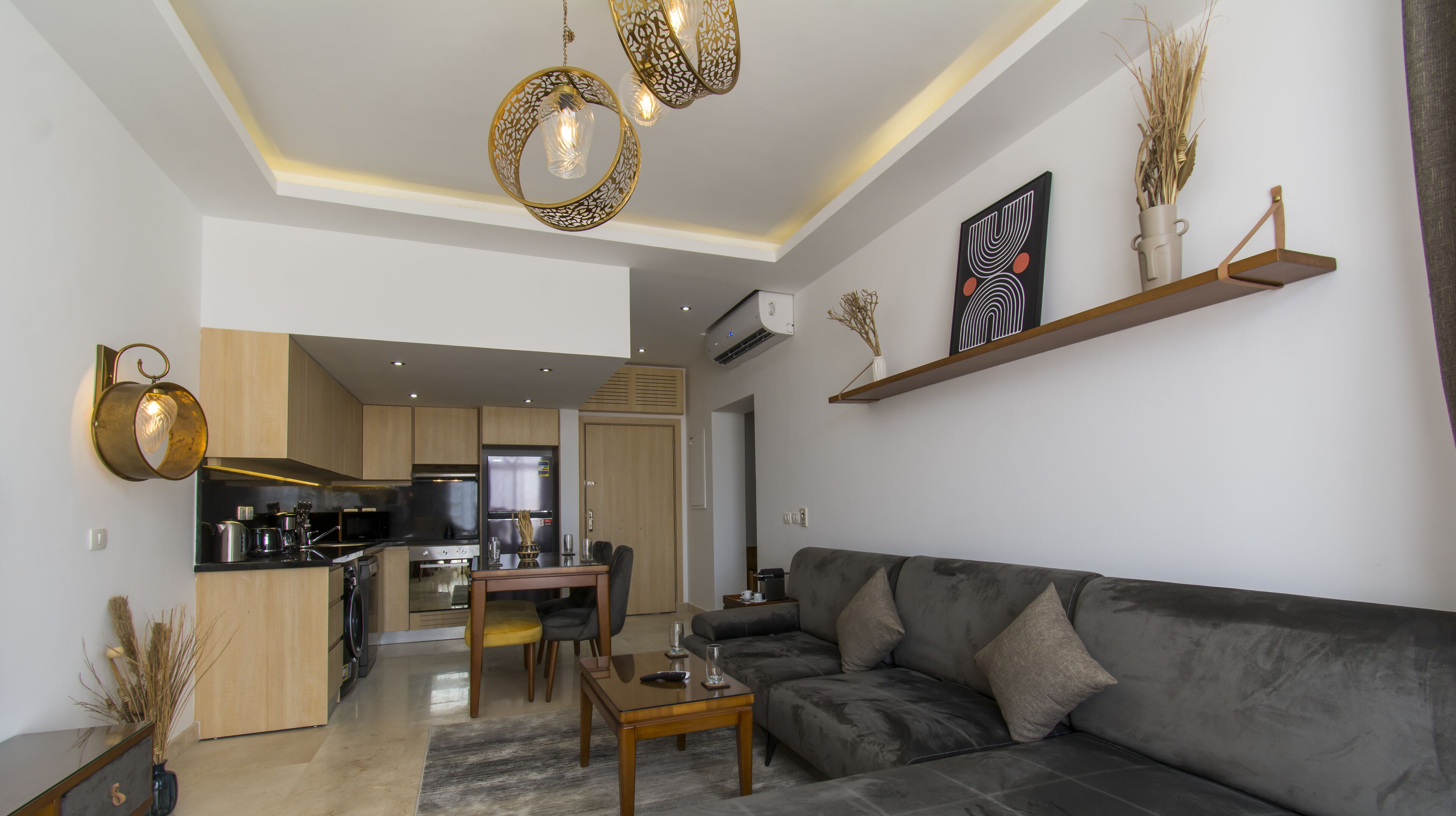 Una sala de estar moderna con un sofá gris, una mesa de centro de madera y un comedor, con una cocina al fondo.
