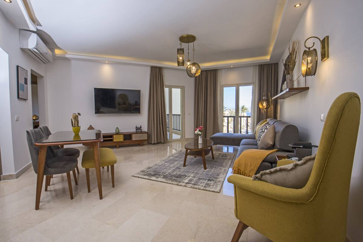A modern living room with a dining area, a sofa, and a TV mounted on the wall.