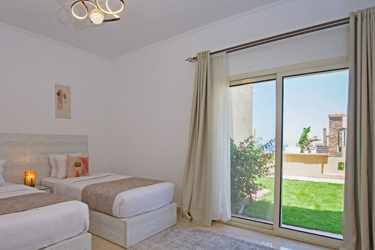 A bedroom with two beds, a large window with curtains, and artwork on the walls.