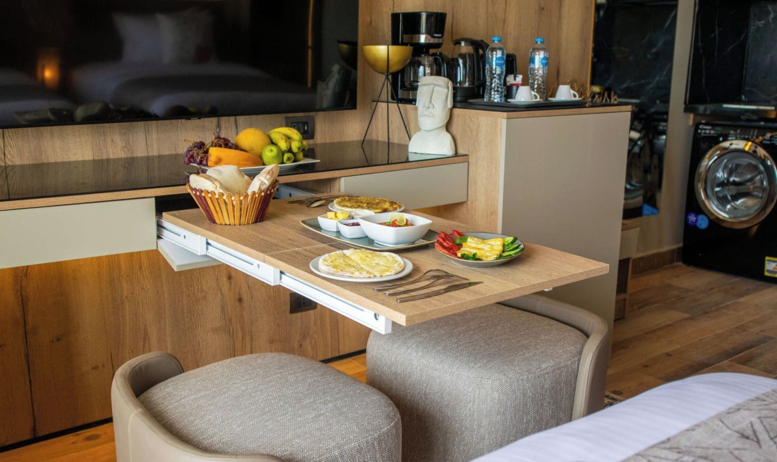 A compact kitchen with a dining area, including a wooden table, chairs, and a variety of food items.