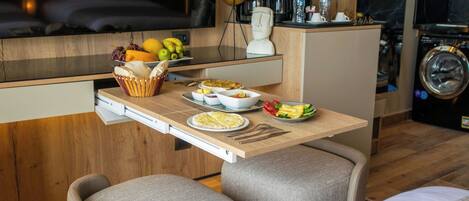 A compact kitchen with a dining area, including a wooden table, chairs, and a variety of food items.