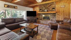 A lodge's living room with a stone fireplace, leather sofas, and a television. - The Dam Overlook  • 3 Min Walk to the Lake • Hot Tub • Game Room (Evergreen)