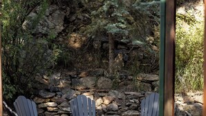 A patio area with Adirondack chairs and a table, surrounded by a stone wall and greenery. - The Dam Overlook  • 3 Min Walk to the Lake • Hot Tub • Game Room (Evergreen)
