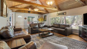 A spacious living room with leather sofas, a wooden coffee table, and a large window offering a view of the outdoors. - The Dam Overlook  • 3 Min Walk to the Lake • Hot Tub • Game Room (Evergreen)