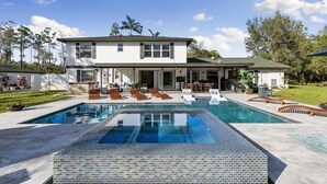 Una casa moderna de dos pisos con una amplia piscina rectangular al frente.