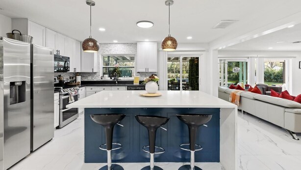 Una cocina moderna con una isla central, taburetes de bar, electrodomésticos de acero inoxidable e iluminación colgante.