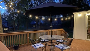 A wooden deck with a round table and chairs, an umbrella, and string lights. - Country Club Charm (Omaha)