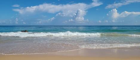 A beach with waves, clear sky, and clouds.