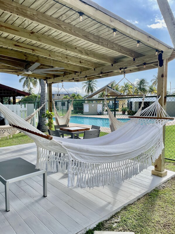 A hammock under a wooden pergola with a pool in the background.