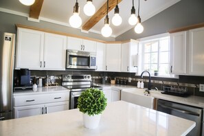 Une cuisine moderne avec des meubles blancs, des appareils en acier inoxydable et un îlot central agrémenté d’une plante en pot.