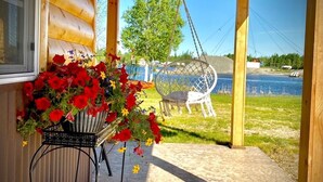 A wooden cabin with a porch, a hanging chair, and a view of a lake. - Newly constructed cabin on a quiet residential pond.  (North Pole)