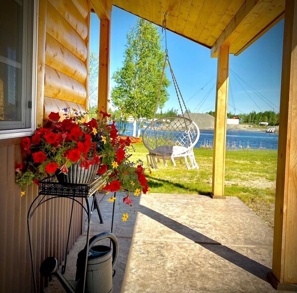 Une cabane en bois avec une véranda, un fauteuil suspendu et une vue sur un lac.