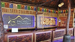 A wooden reception desk with a sign reading "Phí Phí Phu Chalot Beach" and a wall with a decorative pattern. - Phi Phi Phu Chalet Beach Resort (Ko Phi Phi)