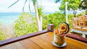 A tropical drink on a wooden table with a view of the ocean and greenery. - Phi Phi Phu Chalet Beach Resort (Ko Phi Phi)