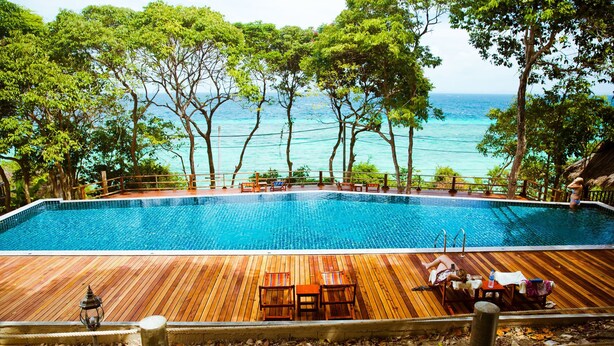 A swimming pool with wooden deck seating and a view of the ocean. - Phi Phi Phu Chalet Beach Resort (Ko Phi Phi)
