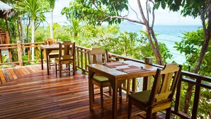 A wooden deck with a table and chairs, overlooking a coastal area with trees and the sea. - Phi Phi Phu Chalet Beach Resort (Ko Phi Phi)