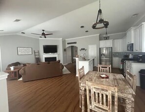 A spacious living room with a brown sofa, a wooden dining table, and a kitchen area with white cabinets and a stainless steel refrigerator. - Immaculate Farmhouse Style Southern Rental (Summerville)
