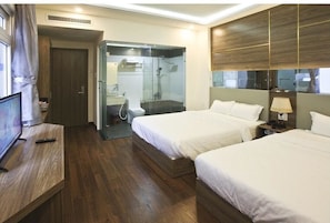 A hotel room with two beds, a TV, a shower area, and a wooden floor.