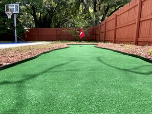 Play a round of golf on our lush artificial turf course, surrounded by trees and a wooden fence.