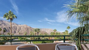 Two metal chairs on a balcony with a view of mountains and palm trees.