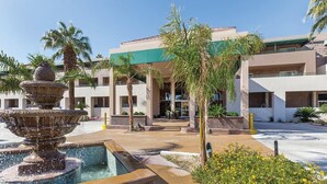 A courtyard with a central fountain, palm trees, and a building with multiple balconies and windows.