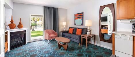 Una camera d'albergo moderna con una moquette fantasia, un divano con cuscini arancioni, un tavolino, un camino e vista sull'esterno.