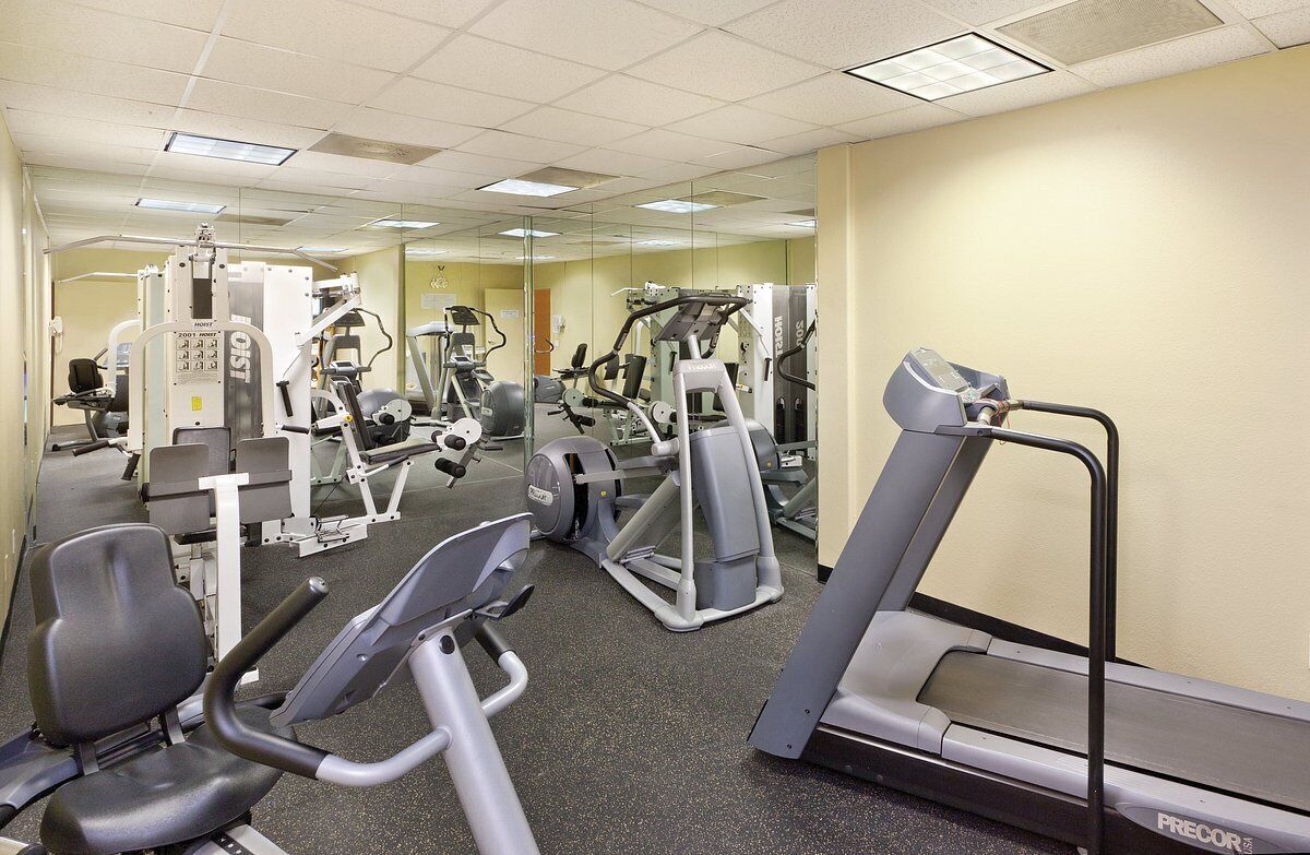 A gym with various exercise machines, including treadmills and weight machines, and a mirrored wall.