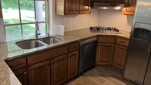 A kitchen with wooden cabinets, a stainless steel sink, a dishwasher, a gas stove, and a refrigerator. - Luxury Lake House  (Atlanta)