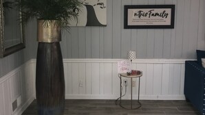 A room with a large potted plant, a framed artwork, a small table with a sign, and a blue upholstered chair. - Luxury Lake House  (Atlanta)