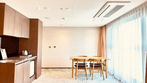 A modern hotel room with a kitchenette, a dining area with two chairs, and a large window with curtains. - Saint Beach Hotel (Jeju City)
