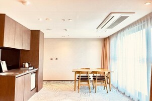 Habitación de hotel moderna con kitchenette, zona de comedor con dos sillas y un ventanal con cortinas.