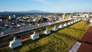 A cityscape with a prominent white fence, a row of white structures, and a distant mountain range. - Saint Beach Hotel (Jeju City)
