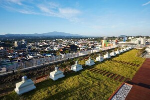 Un paisaje urbano con una valla blanca destacada, una hilera de construcciones blancas y una cadena montañosa distante.