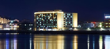 Un hotel de varios pisos con un diseño moderno, ubicado en una esquina destacada y vistas al agua.