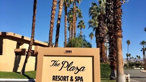 Une enseigne pour le complexe hôtelier et spa The Plaza, avec un ciel bleu clair et des palmiers en arrière-plan.